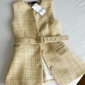 Beige tweedväst med bälte från Zara - Stilren beige väst från Zara i tweed-look med snyggt bälte i midjan och knappar framtill. Västen har en lätt utsvängd form och diskreta fickor 💕Ny med prislapp kvar. Köpt i Spanien för 55eur, säljer för 400sek. 