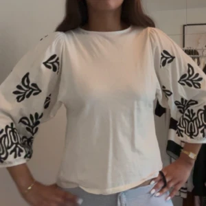 Vit blus med svarta broderade ärmar - Supersnygg vit blus med vida, trekvartsärmar och svart broderat mönster på ärmarna. Bara använd en gång💕Nypris: 399kr 