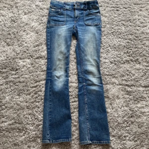 Blå bootcut jeans från H&M - Snygga blå bootcut jeans från H&M med låg midja och justerbar midja. Säljer pågrund av att jag har många andra jeans. Där fram finns en slitning som egentligen inte ska vara där (bild 3) men syns knappt. 