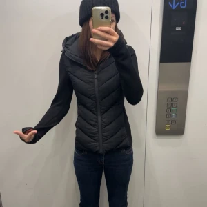 Zara jacka/väst - Säljer en svart pufferjacka med huva och dragkedja framtill. Jackan har quiltad framsida och slimmad passform med långa ärmar. Perfekt för kyliga dagar och enkel att styla till jeans eller tights. Bra skick/s/xs