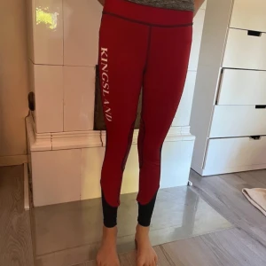 Röda ridleggings från Kingsland - Snygga röda ridleggings från Kingsland med svarta detaljer längs sidorna och vid bensluten. Tight passform och hög midja, Stort vitt Kingsland-tryck på benet och grepp vid knäna