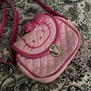 Hello kitty väska - En jätte gullig rosa hello kitty väska som jag köpt här på plick för 3 år sen, säljer den pga jag har bara använt den 1 gång. Den är liten och har lite defekter vid kanterna (bild 4 o 5) men annars är den hel. Ingen aning om vad märket är.