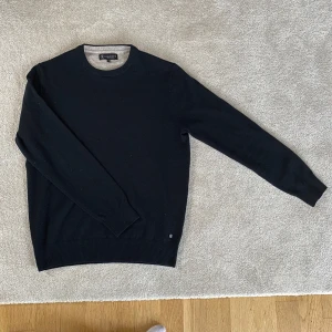 Svart stickad tröja från Lagency extra fine merino wool - Säljer en svart stickad tröja från Lagency i storlek M. Tröjan har rund halsringning, långa ärmar och en liten metallogo vid nederkanten. Perfekt för lager-på-lager och enkel att matcha med det mesta. Merino ull