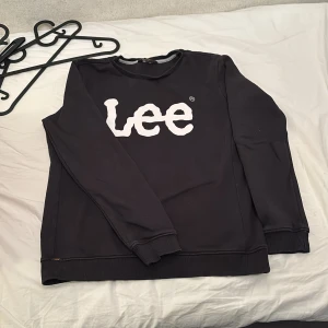 Svart sweatshirt från Lee - Säljer en svart sweatshirt från Lee med stort vitt tryck på bröstet. Tröjan har rund halsringning, långa ärmar och ribbade muddar vid ärmslut och nederkant. Perfekt för en avslappnad stil.
