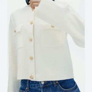 Vit cardigan jacka med guldknappar - Säljer en stilren vit cardigan jacka med raka linjer och dekorativa guldknappar framtill. Jackan har två bröstfickor och lång ärm, perfekt för en clean och modern look.