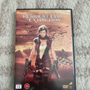 Resident Evil: Extinction DVD - Resident Evil: Extinction på DVD med Milla Jovovich i huvudrollen. Omslaget har en apokalyptisk ökenmiljö med huvudkaraktären beväpnad. DVD-fodralet är svart och filmen är märkt med åldersgräns 15 år. Innehåller special features.