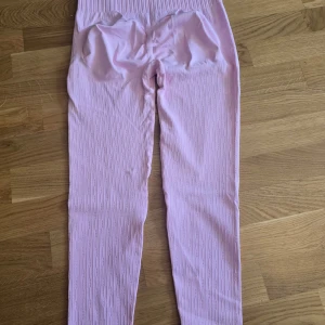 Ljusrosa ribbade leggings - Säljer ett par ljusrosa leggings med ribbad struktur. De har hög midja och är stretchiga, perfekta för en avslappnad stil eller till träning. Snygga att matcha med en oversized hoodie eller crop top.