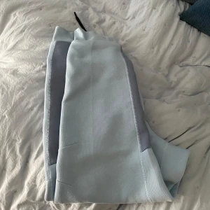 Ljusblå mjukisbyxor från Nike med svarta detaljer - Säljer ett par ljusblå mjukisbyxor från Nike med svarta dragsnören och dragkedja vid fickan. Byxorna har gråa paneler vid underbenen och en vit Nike-logga på låret. Perfekta för en avslappnad stil.