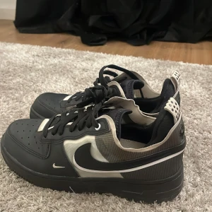 Svarta Nike Air sneakers med vita detaljer - Säljer ett par svarta Nike Air sneakers med vita och grå detaljer. Skorna har klassisk snörning, rund tå och perforerade partier framtill. Swoosh-loggan syns tydligt på sidan och Nike Air-märket på hälen. Perfekta för en sportig och stilren look.