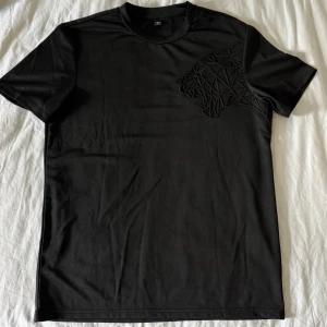 Svart t-shirt med pantermotiv - Svart t-shirt med ett coolt pantermotiv på bröstet. Klassisk rund halsringning och korta ärmar. Perfekt för en clean och modern look.