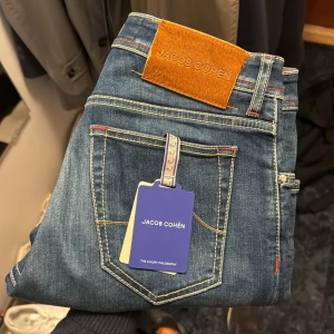 Jacob Cohën jeans  - Snygga blå jeans från Jacob Cohën med klassisk femficksdesign och kontrastsömmar. Byxorna har en läderpatch bak och detaljerad insida med mönstrat tyg. Passformen är rak och de har dragkedja i gylfen.