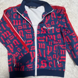 Palm Angels kofta - Denna färgstarka kofta från Palm Angels är i en snygg blå och röd färgkombination med ett iögonfallande mönster. Den är ganska använd men i mycket bra skick, och passar bra i storlek – perfekt för dig som vill sticka ut med en sportig och trendig look.