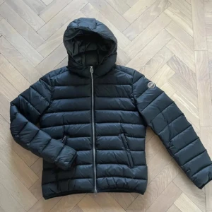 Colmar jacka  - Säljer en svart pufferjacka från Colmar med huva och dragkedja framtill. Jackan har två sidofickor med dragkedja och en diskret logga på ärmen. Perfekt för kyliga dagar. (BYTEN GÖRS)