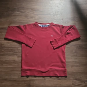 Röd sweatshirt från GANT - Vinröd sweatshirt från GANT med rund halsringning och diskret logga på bröstet. Klassisk modell med långa ärmar och ribbade muddar vid ärmslut och nederkant. Perfekt för en avslappnad stil. Vid frågor eller funderingar hör av dig. Priset är diskuterbart 