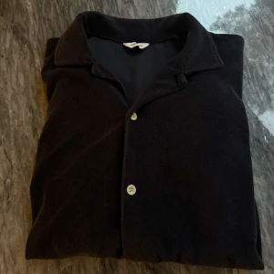 Svart kortärmad skjorta från East West - Säljer en svart kortärmad skjorta från East West med klassisk krage och knäppning framtill. Skjortan har en mjuk känsla och passar perfekt till en avslappnad stil.