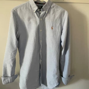 Ljusblå skjorta från Polo Ralph Lauren - Klassisk ljusblå skjorta från Polo Ralph Lauren med button-down krage och broderad logga på bröstet. Slim fit passform och storlek S. 