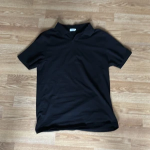 Svart pikétröja från Filippa K - Klassisk svart pikétröja från Filippa K med krage och korta ärmar. Perfekt för en stilren och enkel look. Tillverkad i mjuk bomull som känns skön mot huden.
