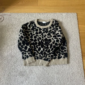 Beige och svart leopardmönstrad stickad tröja från VILA - Säljer en stickad tröja från VILA i beige med svart leopardmönster. Tröjan har rund halsringning, ribbade muddar och är långärmad. Perfekt för dig som vill ha en trendig och mysig look.