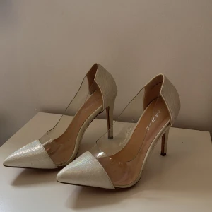 Beige pumps från Sweet Shoes - Säljer ett par eleganta pumps i beige med spetsig tå och transparenta sidor. Skorna har hög klack och har använts ett par gånger men är i ganska bra kondition.