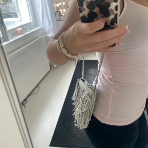 Silver axelväska med fransar - Säljer min snygga fransväska i silver med flätat axelband. Den är liten men rymmer det viktigaste och är i gott skick! Pris kan diskuteras🥰