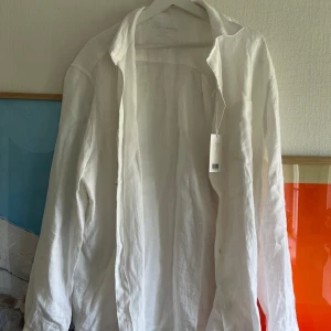 Linneskjorta A Days March - Säljer en klassisk vit skjorta i linne från A Days March. Skjortan har lång ärm, krage och knappar framtill. Perfekt för en stilren och avslappnad look. Linnematerialet gör den sval och skön. 100% linne och helt oanvänd.