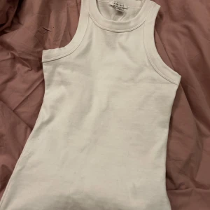 Vit ribbad linnetopp från Amisu - Den är ny! Säljer en klassisk vit ribbad linnetopp från Amisu i storlek XS. Toppen är ärmlös med rund halsringning och har en enkel, stilren design som passar till mycket. Perfekt basplagg i garderoben