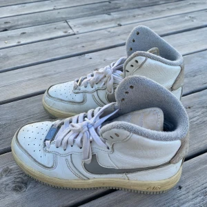 Vita höga Nike Air Force sneakers - Säljer ett par klassiska vita Nike Air Force sneakers med högt skaft och grå detaljer. Skorna har snörning, rund tå och platt sula✨🤗
