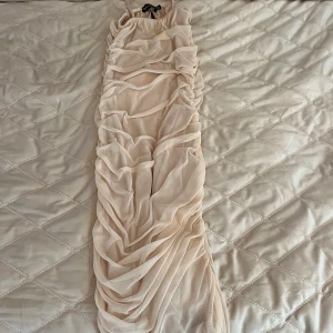 Ljusrosa/beige tklänning från PrettyLittleThing - Säljer en snygg beige midiklänning från PrettyLittleThing med smala axelband och draperad design. Klänningen har en figurnära passform och är tillverkad i ett lätt, transparent material med ett ”undertyg” som ger en elegant look.