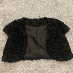 Jätte fin glittrig bolero - Jag säljer denna jätte fina och gulliga svarta boleron med struktur/blommönster. Boleron är i storleken 146/152 men passar en xs. Den är från Lindex kids och är i väldigt bra skick.
