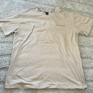 Beige t-shirt med text - En basic beige t-shirt med liten text 'TIME FOR HAPPINESS' på bröstet. T-shirten har rund hals och korta ärmar, perfekt för en avslappnad stil.