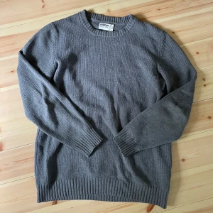 Grå stickad tröja från Dobber - En klassisk grå stickad tröja från Dobber med rund halsringning och ribbade muddar vid ärmslut och nederkant. Perfekt för lager-på-lager och passar till många olika stilar.