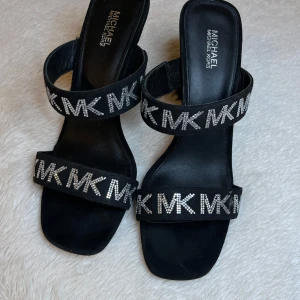 Michael Kors klackskor - Säljer ett par svarta sandaler med klack från Michael Kors. Skorna har två breda remmar med glittrande MK-logga i strass och öppen tå. Perfekta för dig som vill sticka ut med en lyxig touch. Säljer pågrund av att de är för små för mig är storlek 40 och de är 38. Pris kan såklart diskuteras(de är limited edition men har ingen användning till de så priset kan bli billigare)💕va inte rädda för att skriva hur mycket ni är villiga att betala🫶🏼