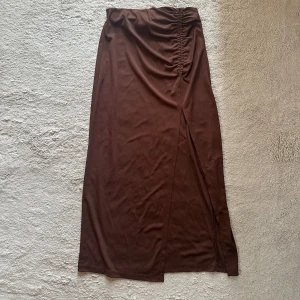 Brun lång kjol - Säljer en brun kjol som går ner till anklarna, den har en slits på framsidan och även rynkande detaljer.