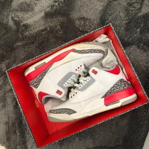 Nike Air Jordan 3 Retro White/Red - Säljer ett par Nike Air Jordan 3 Retro i vitt med röda och grå detaljer. Skorna har klassisk siluett, snörning och ikoniskt elefantmönster på tån och hälen. Perfekta för dig som gillar streetwear och sneakers med attityd.