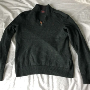 Mörkgrön merinoullströja med halv dragkedja från Morris - Säljer en mörkgrön tröja från Morris i 100% merinoull. Tröjan har halv dragkedja vid halsen och en broderad logga på bröstet. Perfekt för kyligare dagar och har en klassisk, stilren look.