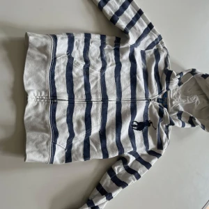  hoodie från Polo Ralph Lauren - Säljer en vit och marinblå randig hoodie från Polo Ralph Lauren med dragkedja och fickor framtill. Tröjan har långa ärmar och klassisk broderad logga på bröstet. Perfekt för en avslappnad stil.