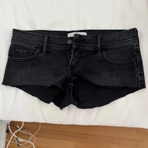 Lågmidjade jeansshorts - Ett par jättefina grå/svarta lågmidjade jeansshorts från hollister. Storlek 26 vilket passar mig som brukar ha xs/s. Använda men i fint skick 💘💘De är vintage och går inte att köpa längre. 