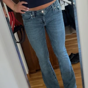True Religion ljusblå jeans - Säljer ett par klassiska ljusblå jeans från True Religion med bootcut och snygga detaljerade bakfickor. Jeansen har normal passform och är tillverkade i denim med ikoniska sömmar och logga på bakfickan. Är low waist och true to size, själv bär jag oftast medium och är 162 cm lång (byxorna är lite långa på mig)