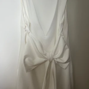 Vit klänning från YAS - Elegant vit klänning från YAS med en stor rosett baktill. Klänningen har en v-ringad design och är ärmlös, perfekt till studenten!! Nypris: 1300