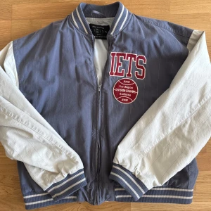 Grå och vit bomberjacka från Urban Outfitters - Säljer en snygg bomberjacka från Urban Outfitters i grått och vitt. Jackan har en dragkedja framtill och ribbade muddar vid ärmslut och nederkant. Finns någon liten fläck på armen som går att tvätta bort. Cond 9/10