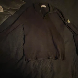 Svart tröja med dragkedja från Stone Island - Säljer en stilren svart tröja från Stone Island med dragkedja och lång ärm. Tröjan har en broderad logotyp på ärmen och ribbade kanter. Perfekt för en avslappnad och trendig look.kan gå ner i pris vid snabbt köp