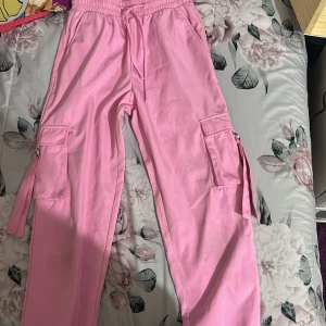 Rosa cargopants med snörning - Säljer ett par rosa cargopants med elastisk midja och snörning. Byxorna har praktiska fickor på sidorna och dekorativa band. Perfekta för en avslappnad stil.