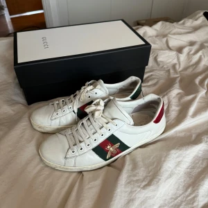 Gucci Sneakers - Snygga från Gucci med klassiska gröna och röda ränder på sidan och broderat bi. Skorna har snörning och en rund tå. Baktill finns röda och gröna detaljer med Gucci-logga, något flagna baktill. Kvitto, dustbox och låda finns.