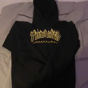 Säljer en svart hoodie från Thrasher med den ikoniska loggan i gult och flammor. Perfekt för streetwear-stilen och sköna dagar. Huvan har dragsko och tröjan är i en mjuk och bekväm bomullsmix.