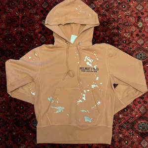 [Helmut Lang] Hoodie - HELMUT LANG HOODIE. Tröjan är i mint condition, knappt använd. Köpt på Vestaire Collective för 1800 och säljs nu vidare för då den inte kommer till använding. Tröjan är i en terracotta orange färg och har paint splatter runt om. Storlek S 
