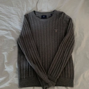 Grå ribbad tröja från Gant - Säljer en stilren grå ribbad tröja från Gant. Tröjan har en klassisk rund halsringning och långa ärmar. Perfekt för kyligare dagar och passar till det mesta i garderoben.