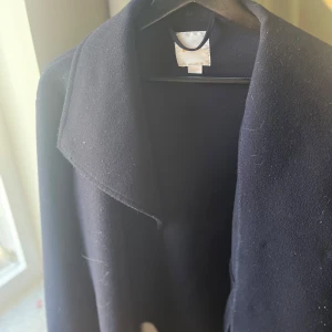 marinblå kappa - Elegant marinblå kappa med klassisk design och bred krage. Perfekt för dagar när det är lite kyligt men även när det är varmt och ger en stilren look. Passar bra till både vardag och mer formella tillfällen.