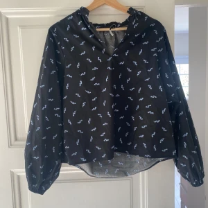 Långärmad blus från neo noir - Svart blus med supergulligt mönster av små ljusblåa blommor. Puffiga ärmar och super fin att ha när man ska vara lite uppklädd. Endast använd en gång och är i nyskick med inga defekter. 