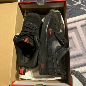 Nike Air Force 1 Low Multi - Snygga svarta Nike Air Force 1 Low med orange detaljer. Skorna har en klassisk design med snörning och en robust sula. Perfekta för dig som vill ha en stilren look med en färgklick.