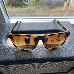 Turtle-mönstrade solglasögon från Ray-Ban - Snygga turtle-mönstrade solglasögon från Ray-Ban med klassisk design. Bågarna har en brun och svart leopardmönstrad finish och glasen är tonade. Perfekta för en stilren look. Obs ej orginal